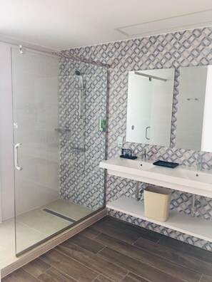 A modern bathroom with a glass shower enclosure, a white vanity with a mirror, and patterned wall tiles.