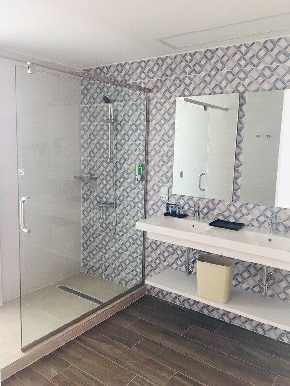A modern bathroom with a glass shower enclosure, a white vanity with a mirror, and patterned wall tiles.