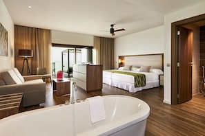 Un hotel moderno con una bañera grande, un sofá, un escritorio, una cama con cabecera y vistas a través de una puerta de cristal.