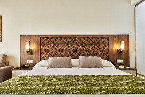 Habitación de hotel con una cama grande, dos mesitas de noche, una mesilla auxiliar, un plaid verde con estampado y un diseño geométrico en la pared.