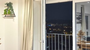 A room with a balcony door open, a view of a cityscape at night, a small shelf with decorative items, and a curtain partially drawn. - City Centre - Apt - Sleeps4 - Canal View - Parking (West Midlands)