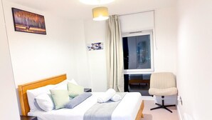 A neatly arranged hotel room with a bed, a chair, a nightstand, a window with curtains, and a painting on the wall. - City Centre - Apt - Sleeps4 - Canal View - Parking (West Midlands)