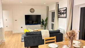 A modern living room with a sofa, TV, dining table set for two, and a large window with curtains. - City Centre - Apt - Sleeps4 - Canal View - Parking (West Midlands)