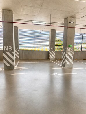 Un estacionamiento vacío con pilares de concreto marcados N3, una barrera metálica rayada y vista de un edificio con líneas horizontales.