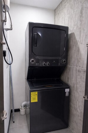 Una lavadora y secadora compactas con panel de control, una etiqueta de advertencia amarilla y un tubo de ventilación metálico.