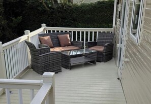 Een overdekt terras met rieten meubels en een glazen tafel.