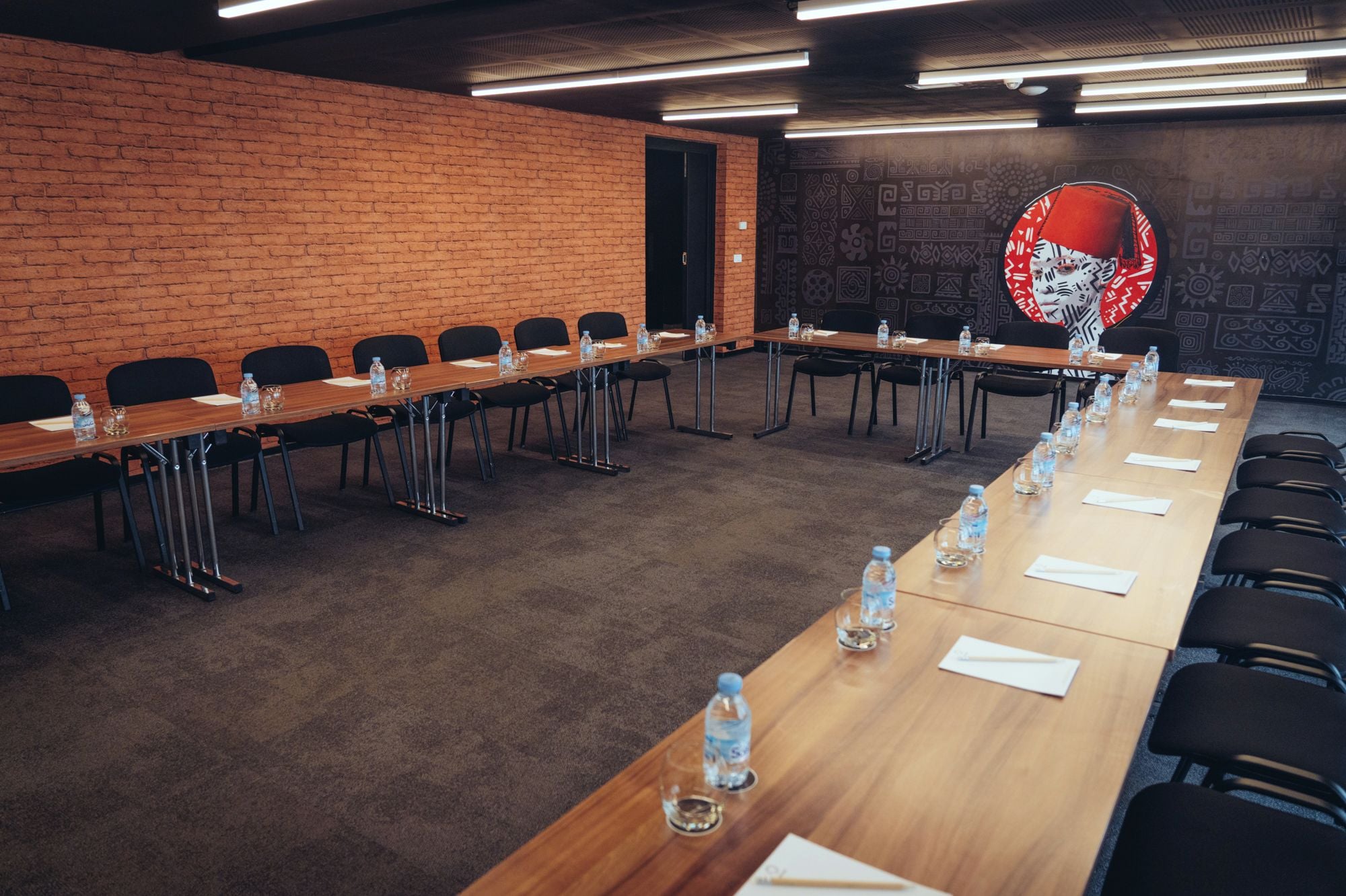 Sala de conferências com uma mesa comprida, cadeiras, garrafas de água e uma parede de tijolos.