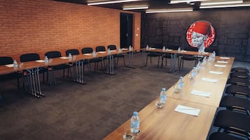 Sala de conferências com uma mesa comprida, cadeiras, garrafas de água e uma parede de tijolos.