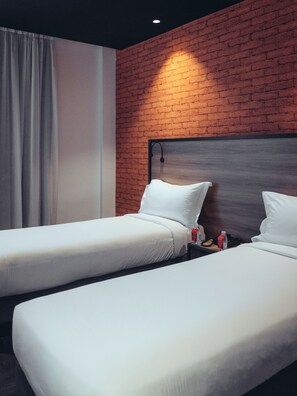 Quarto de hotel com duas camas de solteiro, uma parede de tijolos e cortina.