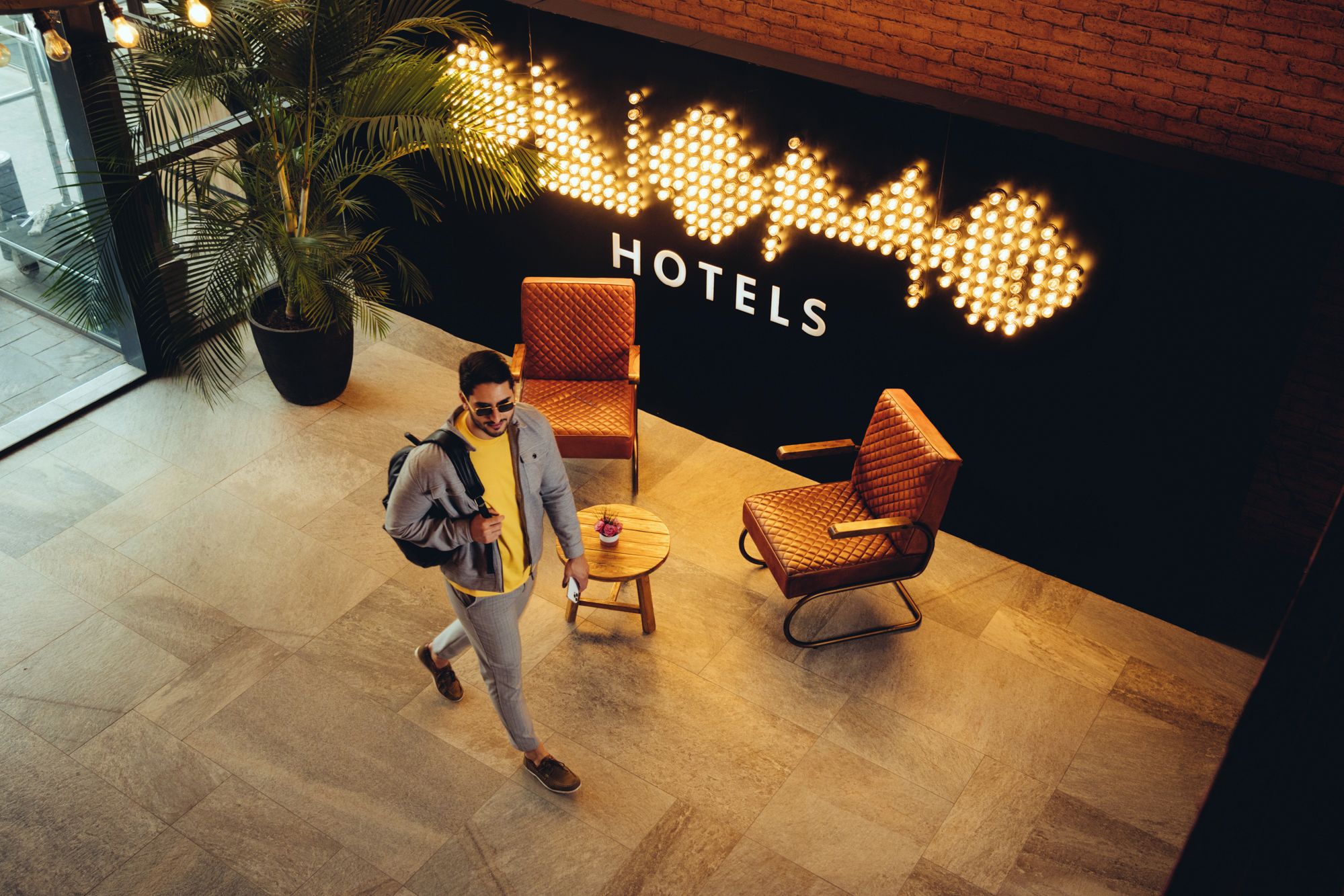 Un hall d'hôtel au design moderne, avec une grande enseigne sur laquelle est inscrit le mot « HÔTELS » et un luminaire décoratif placé au-dessus. On y trouve deux espaces de détente avec des fauteuils confortables et une petite table ronde.