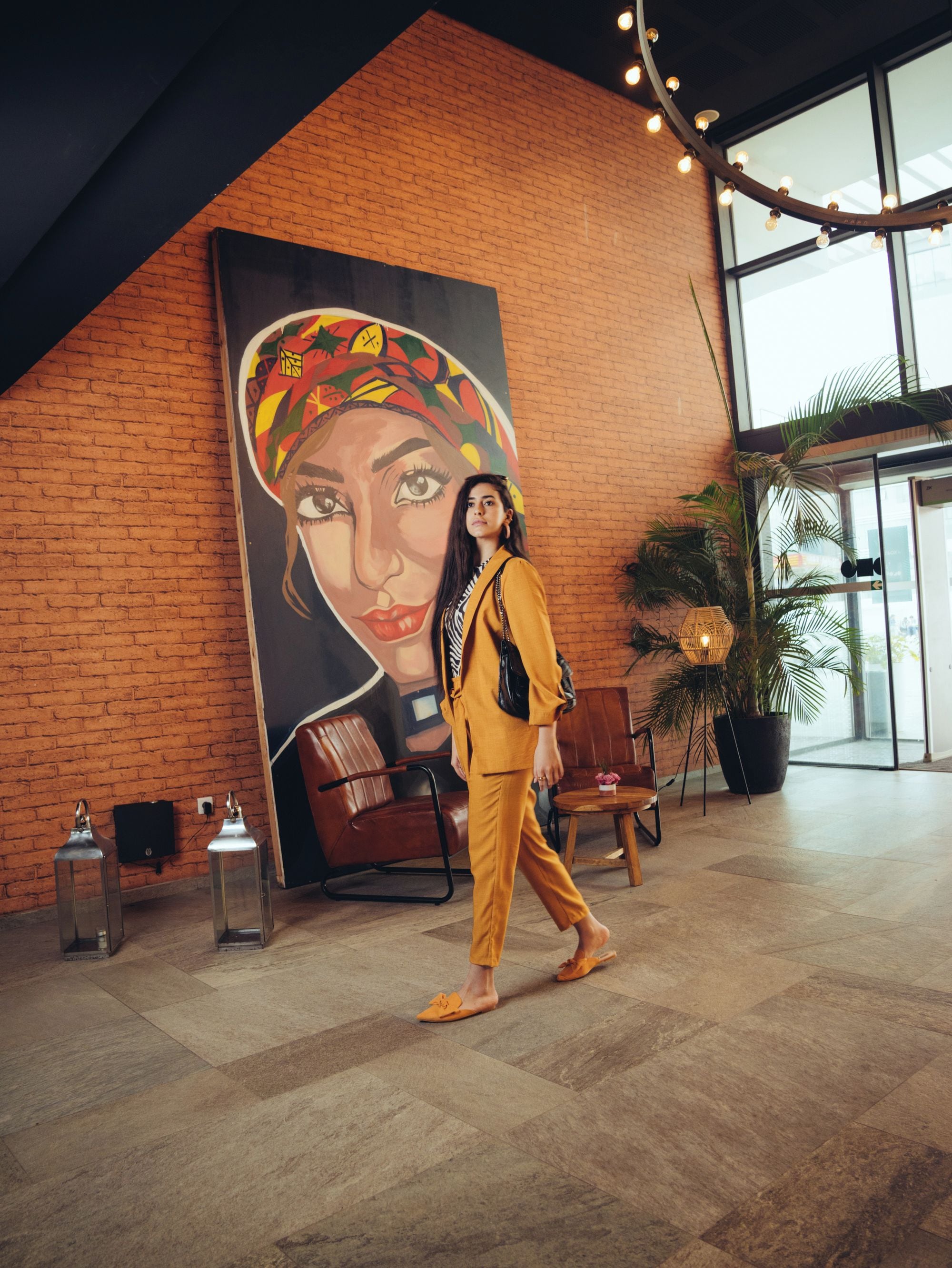 Une personne se promène dans un hall d’entrée orné d’une grande fresque murale, avec un mur en briques et une grande fenêtre.