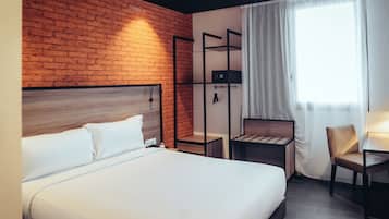 A hotel room with a brick wall, a bed, a desk, and a chair.