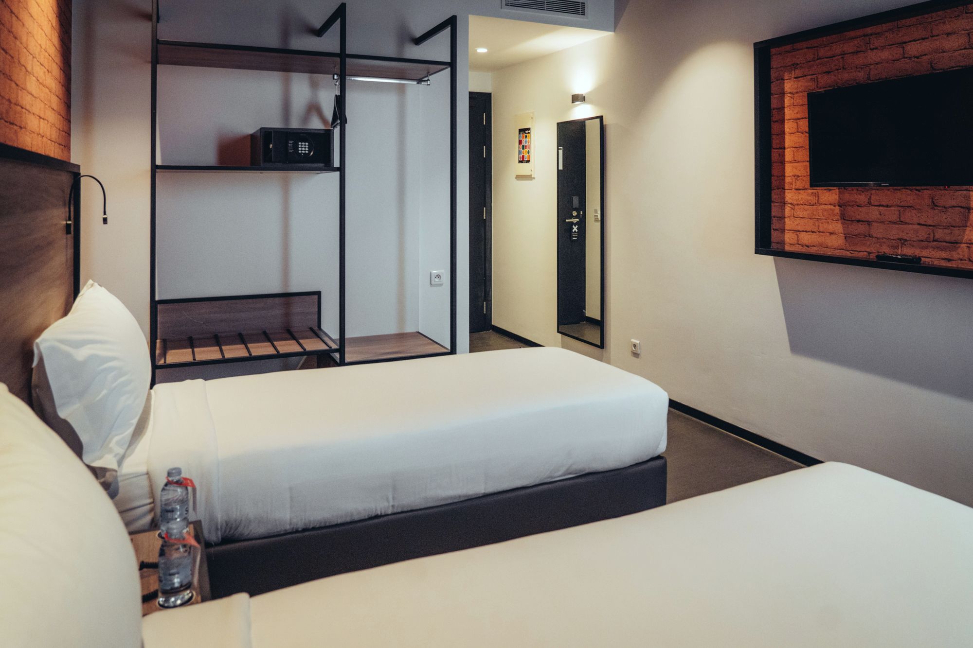 Una habitación de hotel con dos camas, un televisor montado en la pared y un minibar.