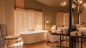 Un baño moderno con una bañera independiente, un tocador con un espejo grande y una ventana con persianas.