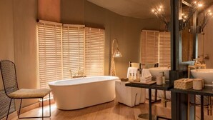A modern bathroom with a freestanding bathtub, a vanity with a large mirror, and a window with blinds. - Banjaar Tola A Taj Safari Kanha National Park (Bichhiya)