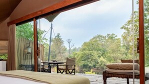Una habitación tipo tienda de campaña con una cama, una mesa y sillas, y vistas al exterior.