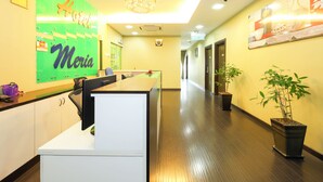 A hotel reception area with a reception desk, a green sign with the name 'Maria,' a chandelier, and a hallway with doors and potted plants. - Super OYO Capital O 812 Hotel SMC Seksyen 13 (Shah Alam)