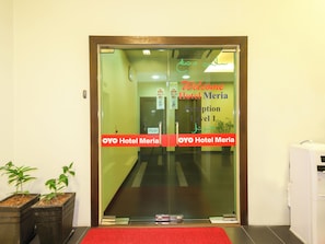 A hotel reception area with a glass door, a red carpet, and two potted plants.