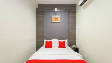 A hotel room with a bed, a nightstand, an air conditioning unit, and a wall-mounted picture.