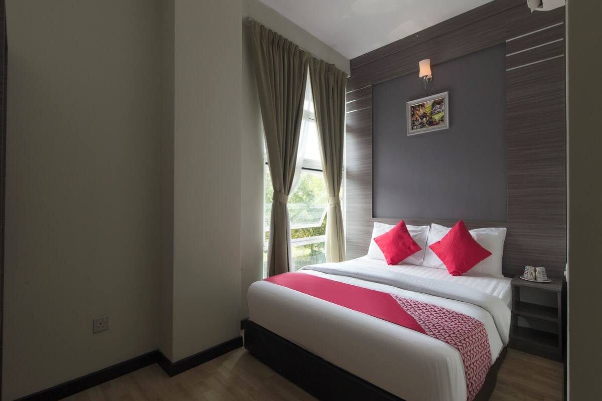 Ein Hotelzimmer mit einem großen Bett, einem Nachttisch, einer Wandleuchte und einem Fenster mit Vorhängen.