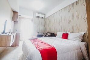 A hotel room with a bed, a desk, and an air conditioning unit. - Reddoorz Apartment @ Green Lake View Ciputat (Jakarta)