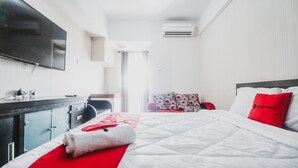 A hotel room with a bed, a desk, a chair, a TV, and an air conditioning unit. - Reddoorz Apartment @ Green Lake View Ciputat (Jakarta)