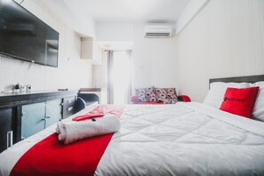 A hotel room with a bed, a desk, a chair, a TV, and an air conditioning unit. - Reddoorz Apartment @ Green Lake View Ciputat (Jakarta)