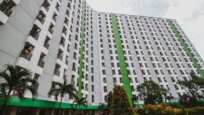 A high-rise building with a grid of balconies, a green lower section, and a landscaped area with trees and shrubs. - Reddoorz Apartment @ Green Lake View Ciputat (Jakarta)