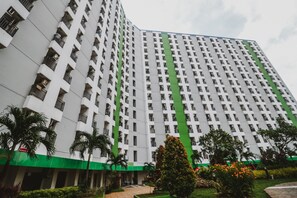 A high-rise building with a grid of balconies, a green lower section, and a landscaped area with trees and shrubs. - Reddoorz Apartment @ Green Lake View Ciputat (Jakarta)