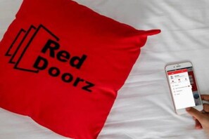 A pillow with 'Red Doorz' text and a smartphone displaying a hotel booking page. - Reddoorz Apartment @ Green Lake View Ciputat (Jakarta)