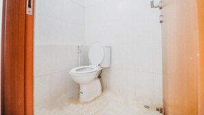 A small, white-tiled bathroom with a white toilet, a wooden door frame, and a visible drain. - Reddoorz Apartment @ Green Lake View Ciputat (Jakarta)