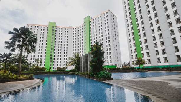 A modern hotel with a pool, surrounded by greenery and tall buildings. - Reddoorz Apartment @ Green Lake View Ciputat (Jakarta)