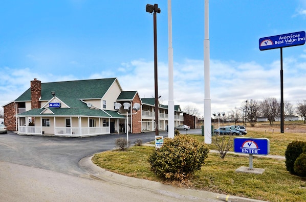 A motel with a green roof, a covered parking area, and a sign indicating it's part of the Americas Best Value Inn chain. - Residential Suites Blue Springs by Hotel O I 70 (Grain Valley)