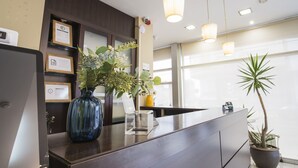 Un mostrador de recepción con un jarrón azul lleno de flores, una planta en maceta e información digital en un quiosco.