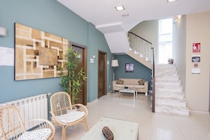 A modern interior with a staircase, a sofa, two wicker chairs, a coffee table, and a large abstract painting. - Alda Barraña Playa (Boiro)