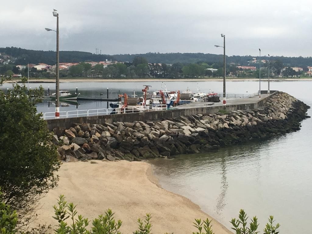 A pier with boats and construction equipment, a sandy beach, and a rocky shoreline.