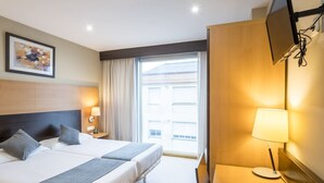 Una habitación de hotel con cama, lámparas de noche, televisión y ventana con cortinas.