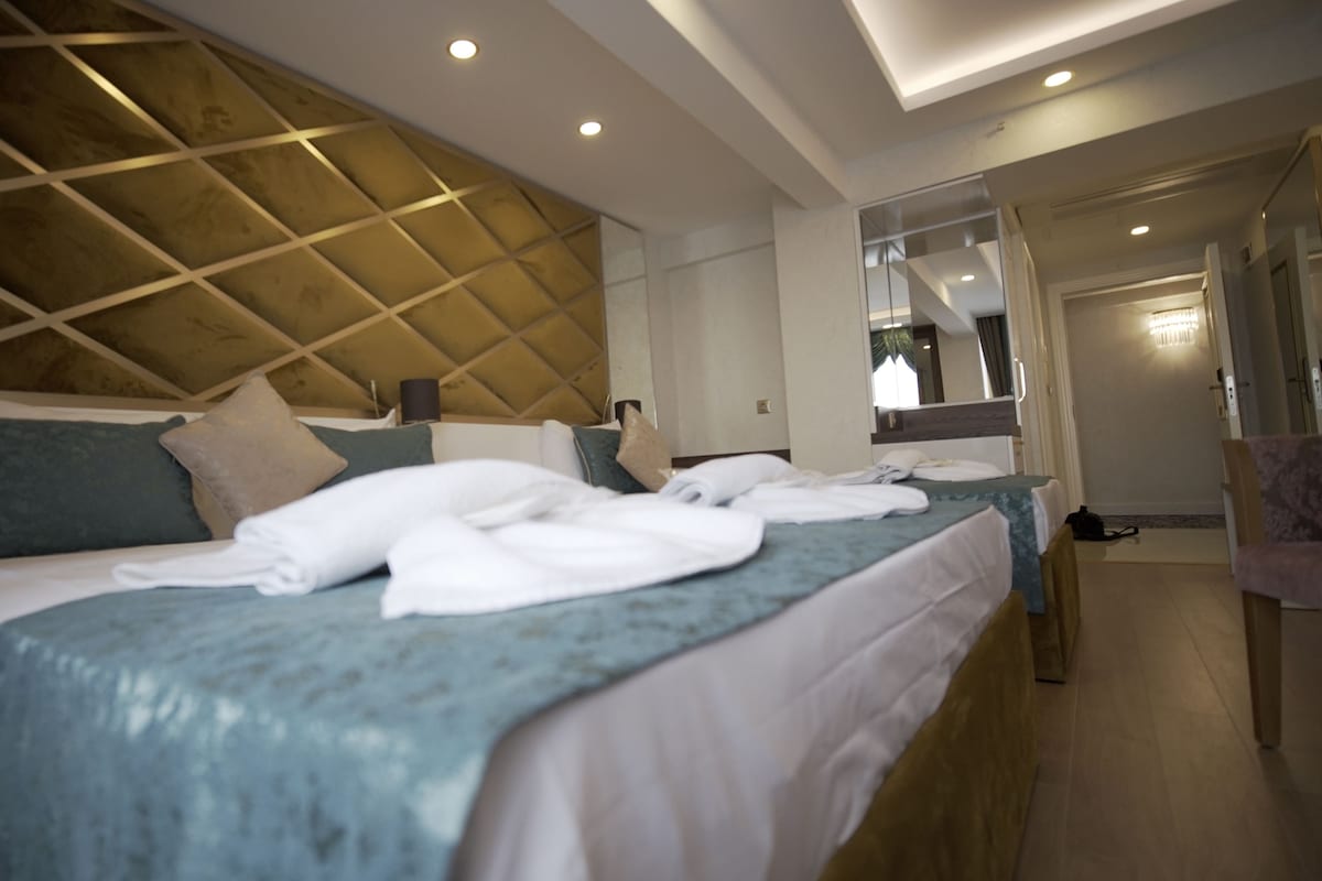 Une chambre d’hôtel avec un grand lit, une tête de lit en bois, un miroir et une salle de bain visible à travers une porte ouverte.