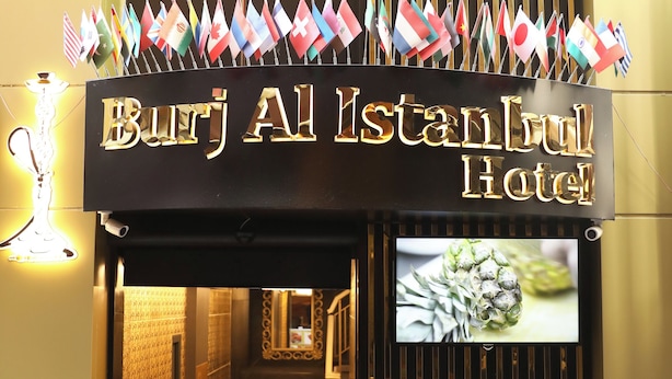 La entrada del Hotel Burj Al Istanbul, con un cartel, banderas, una pantalla de televisión y una zona de estar.