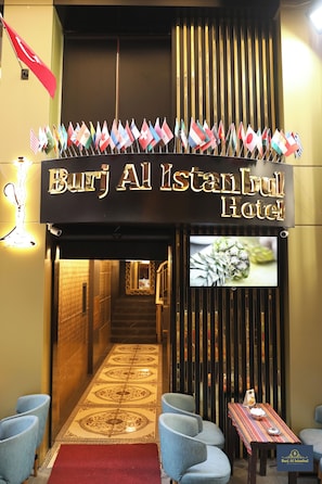 L’entrée de l’hôtel Burj Al Istanbul, avec une enseigne, des drapeaux, un écran de télévision et un espace détente.