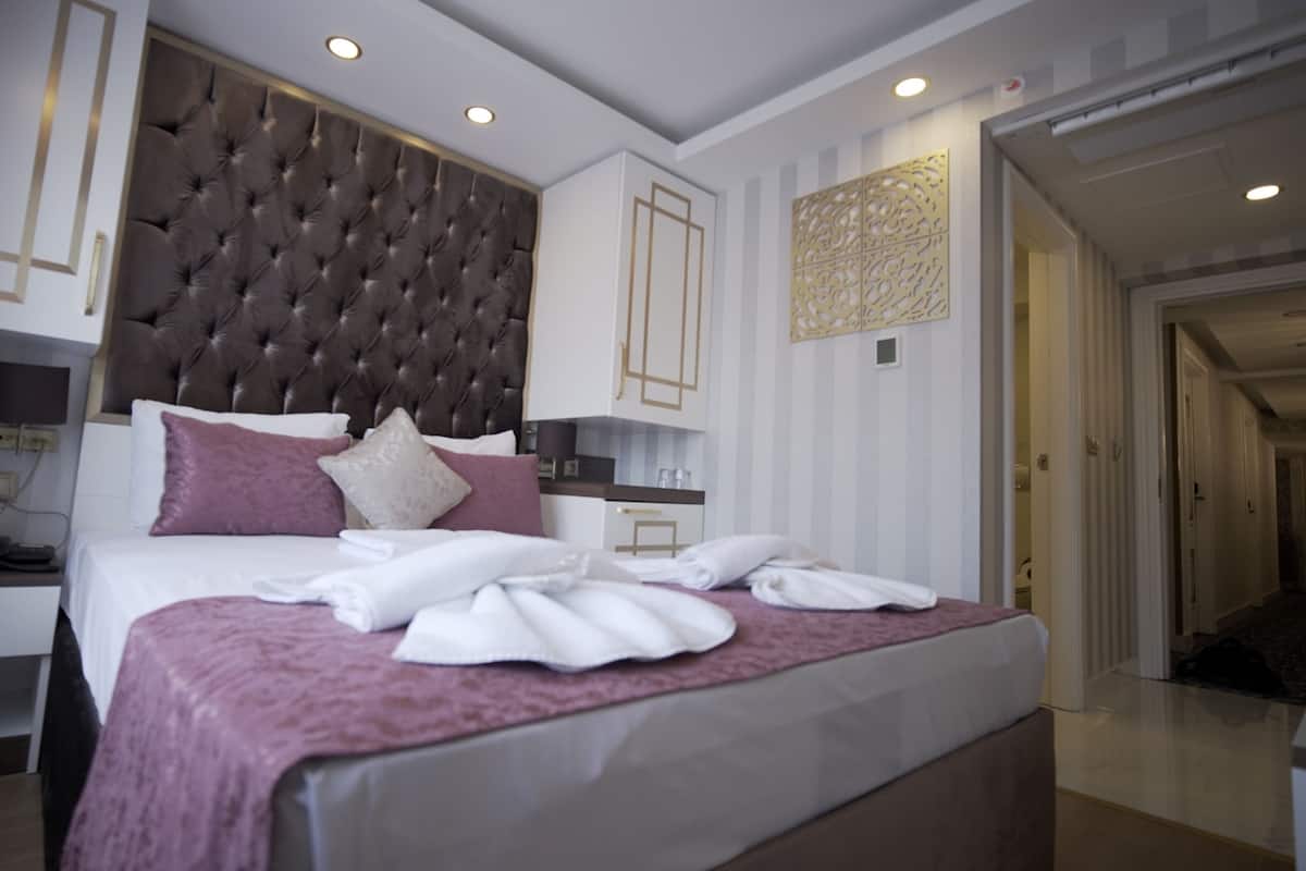 Ein modernes Hotelzimmer mit einem großen Bett, einer festen Kopfteil, einem Nachttisch und einem kleinen Schreibtisch mit Stuhl.