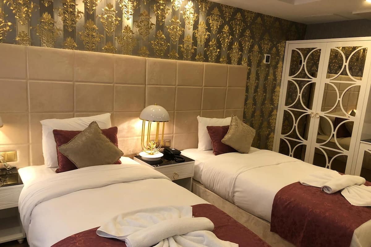 Ein Hotelzimmer mit zwei Betten, einem Nachttisch mit Lampe, einem Telefon und einer dekorativen Wandverkleidung.