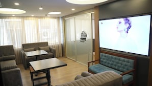 Habitación de hotel con televisión de pantalla plana, un sofá, una mesa y una ventana con cortinas.