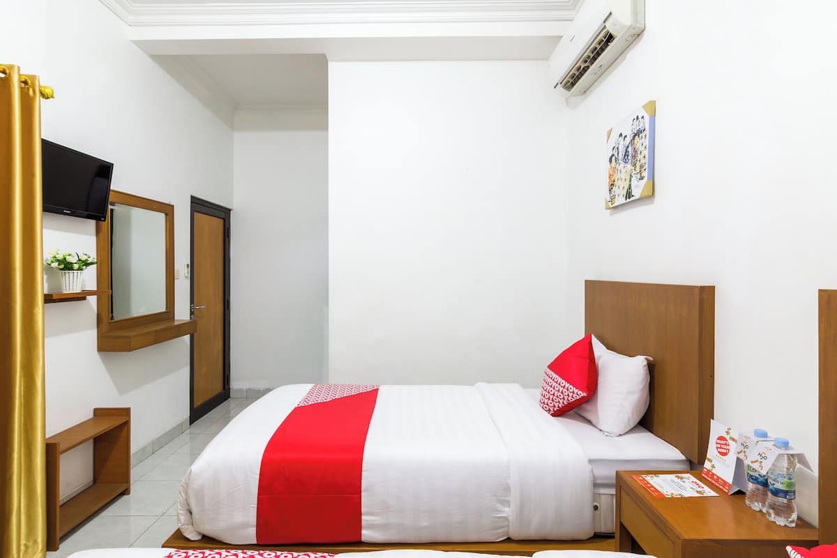 A hotel room with a bed, a bedside table with water bottles, a TV, and a mirror.