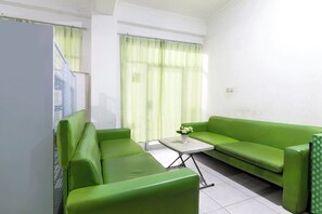 Una habitación con un sofá verde, una mesita con un jarrón y una ventana con cortinas.