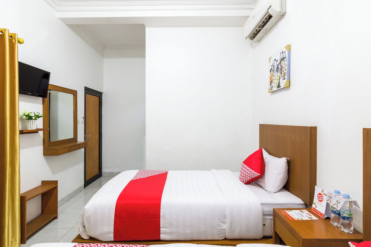 Habitación de hotel con cama, mesita de noche con botellas de agua, televisor y espejo.