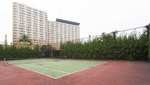A tennis court with a net, surrounded by a red surface, and a building in the background. - Reddoorz Apartment @ Margonda Residence Tower 2 (Depok)
