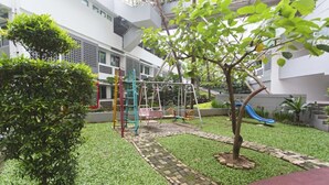 A playground with a slide and climbing structures, surrounded by a well-maintained lawn and a building in the background. - Reddoorz Apartment @ Margonda Residence Tower 2 (Depok)