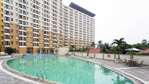 A swimming pool with a tiled deck, surrounded by a high-rise building with multiple balconies. - Reddoorz Apartment @ Margonda Residence Tower 2 (Depok)