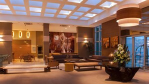 A spacious lobby with a high ceiling, a central seating area, and a large window providing a view of the outside. - Jade Hotel (Guará)